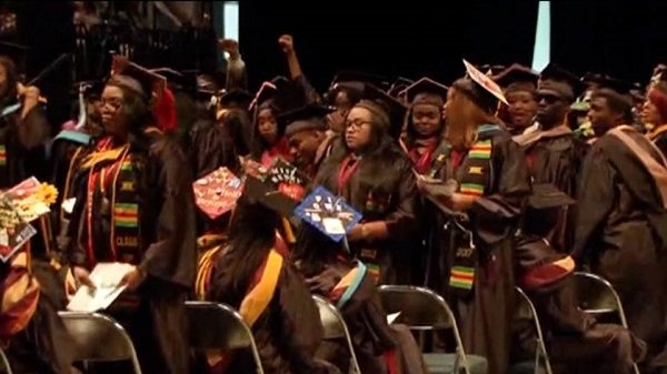 Graduating students stand and turn their backs to Education Secretary during commencement ceremony.
