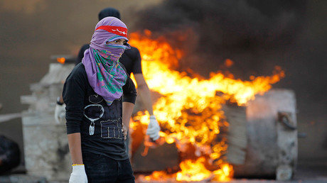A protester holding stones stands next to fire during police clashes in the village of Sitra south of Manama © Hamad I Mohammed
