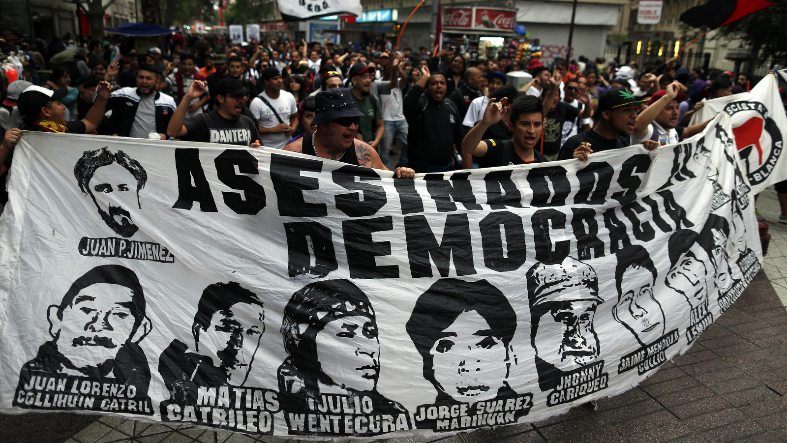 Protesters commemorate the eighth year anniversary of the police killing of Mapuche indigenous activist Matias Catrileo in Santiago, Chile, Jan. 5, 2016, carrying a banner showing the faces of protesters who have died during Chile's democratic governments. (AP/Luis Hidalgo)