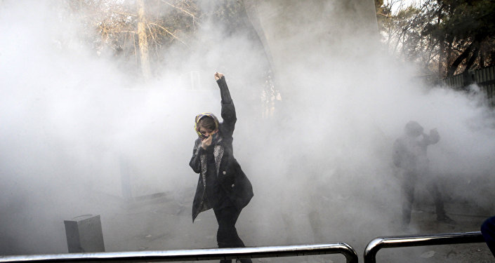 FILE - In this Saturday, Dec. 30, 2017 file photo taken by an individual not employed by the Associated Press and obtained by the AP outside Iran, a university student attends a protest inside Tehran University while a smoke grenade is thrown by anti-riot Iranian police, in Tehran, Iran