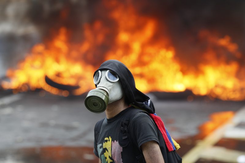An anti-government protester stands in front of burning barricade on a highway in Caracas, Venezuela, Monday, April 24, 2017. Thousands of protesters shut down the capital city's main highway Protesters in least a dozen other cities also staged sit-ins as the protest movement is entering its fourth week. (AP/Ariana Cubillos)