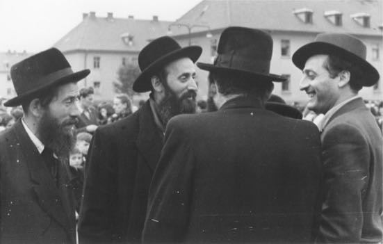 A group of religious Jewish men converse outside at the Bergen Belsen displaced persons camp.jpg