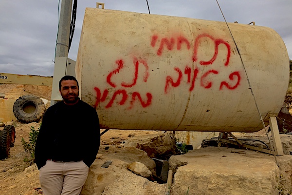Mahmoud, who works in Urif's quarry, stands next to a container that was graffitied by settler youth during a recent spate of hate crimes in the village. The graffiti reads: 'Fight your enemy. Price tag.' (Edo Konrad)