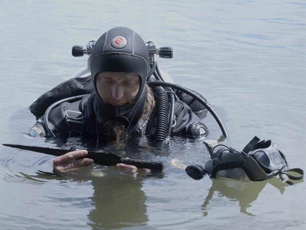 One of the Polish archaeologists surfacing with just one of the 20 artifacts found on the lake bottom, including the rare medieval sword. (Nicolaus Copernicus University)