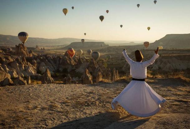 Dervish doing a ritual in Cappadocia with balloons in the background at sunrise. 