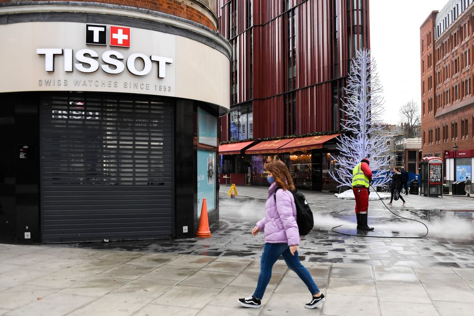 A woman walks past a closed shop while a man cleans the deserted pavement near Oxford Street in London on Tuesday. Oxford Str