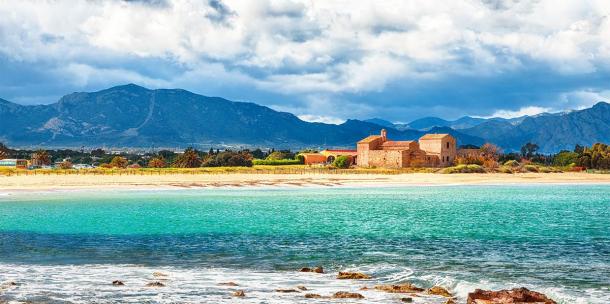 The Nora bay and beach, the medieval Sant'Efisio church near the shore and mountains in the background (pilat666 / Adobe Stock)