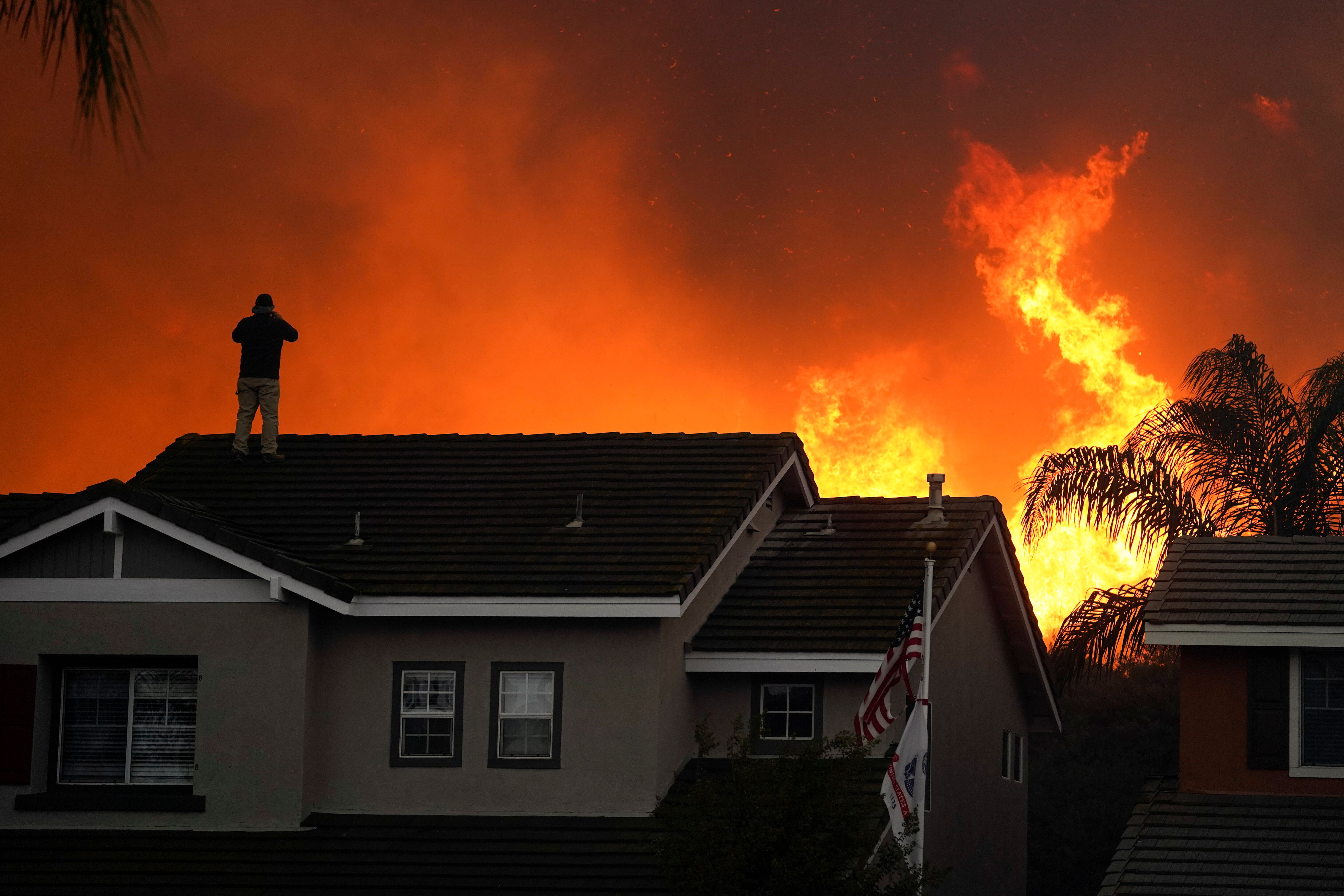 Herman Termeer, 54, stands on the roof of his home as the Blue Ridge Fire burns along the hillside in Chino Hills, Calif., on