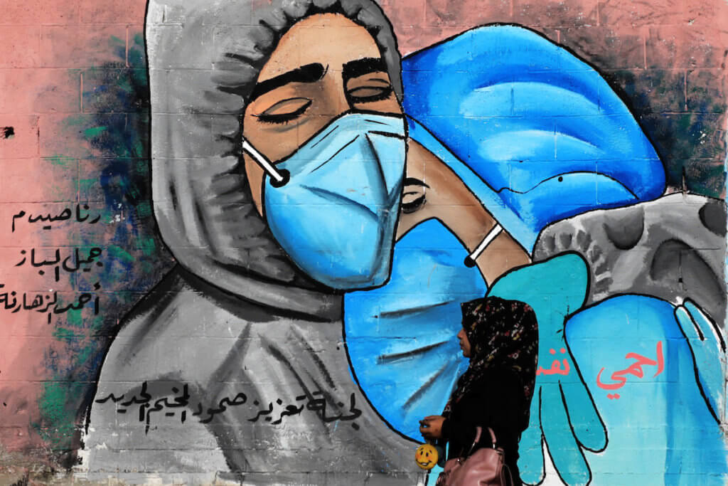 A Palestinian women walks past a mural showing mask-clad mourners in the Nuseirat refugee camp in central Gaza on November 16, 2020. (Photo: Ashraf Amra/APA Images)