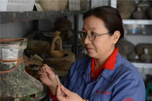 Xu Weihong working on a vase found at the ancient Xianyang site. (Zhang Xiping / China Daily)