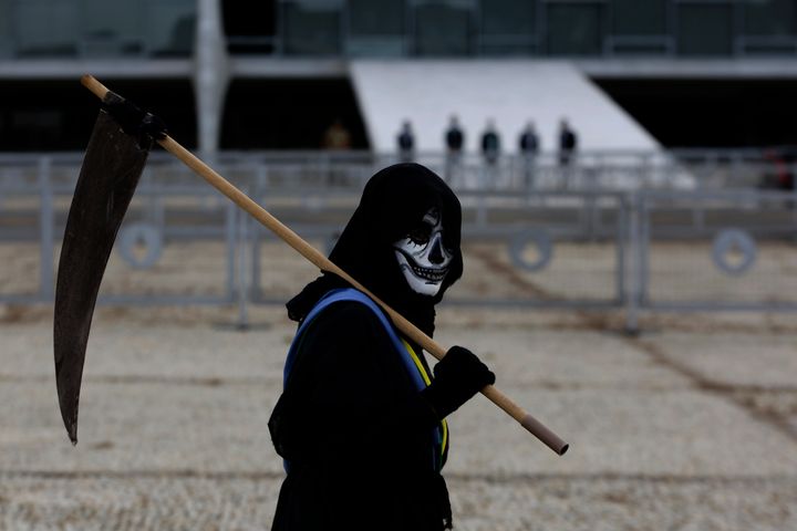 A demonstrator dressed as death and wearing a mock presidential sash walks outside Planalto presidential palace during a prot