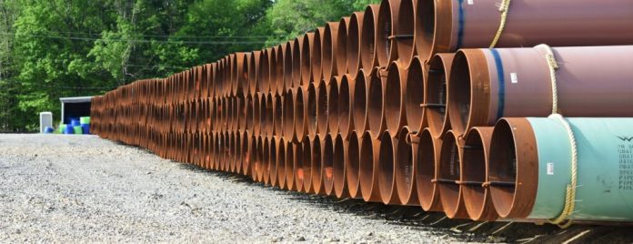 Rust-red and turquoise pipe sections are stacked three high on gravel in a wood part of Ohio.