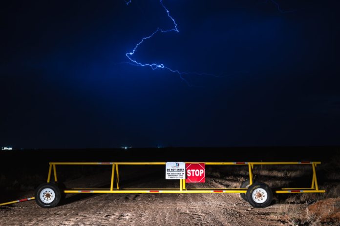 Lightning strikes over Lotus LLC disposal facility mobile gate with a stop sign over a dirt road. 