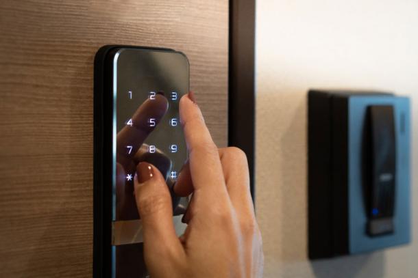 Closeup of a woman's finger entering the password code on a smart digital touch screen keypad entry door lock for a hotel room. (myboys.me / Adobe Stock)