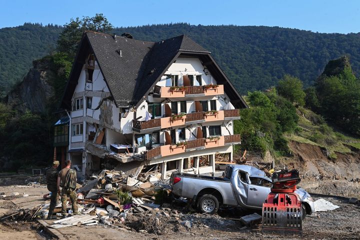 Military personnel stand beside a ruined country guest house in Laach, Germany.