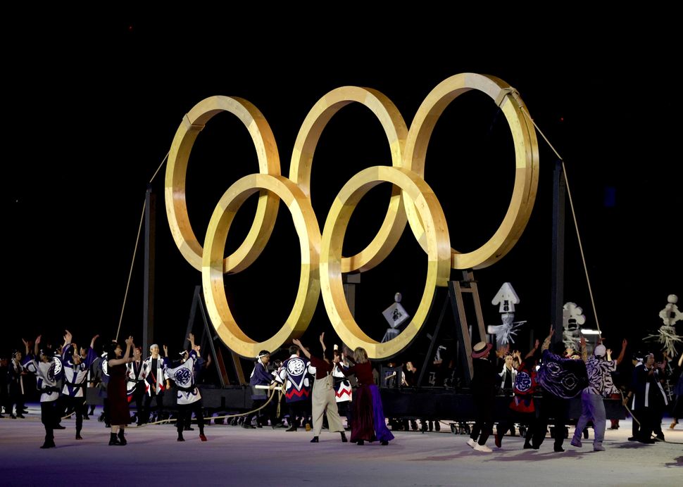 Performers dance in front of giant golden Olympic Rings.