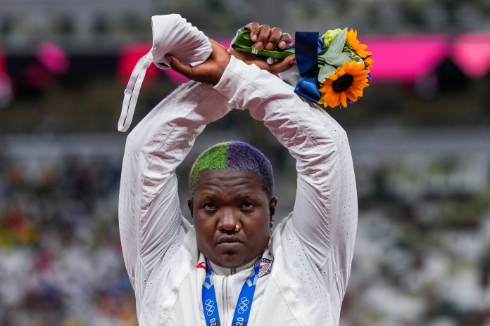Woman stands wearing silver medal making an X above her forehead