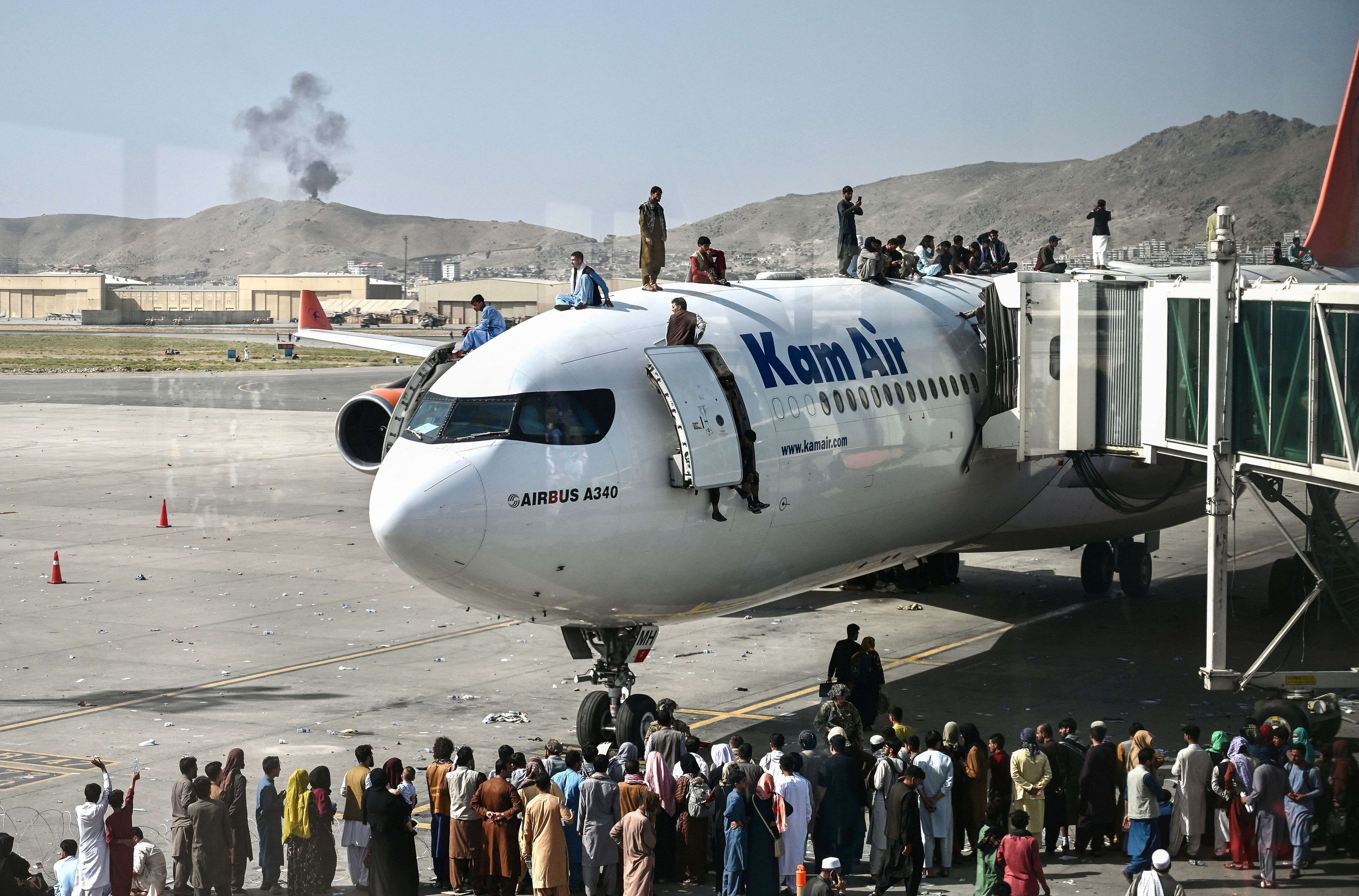 Afghan people climb atop a plane as they wait at the Kabul airport in Kabul on Aug.16, 2021.