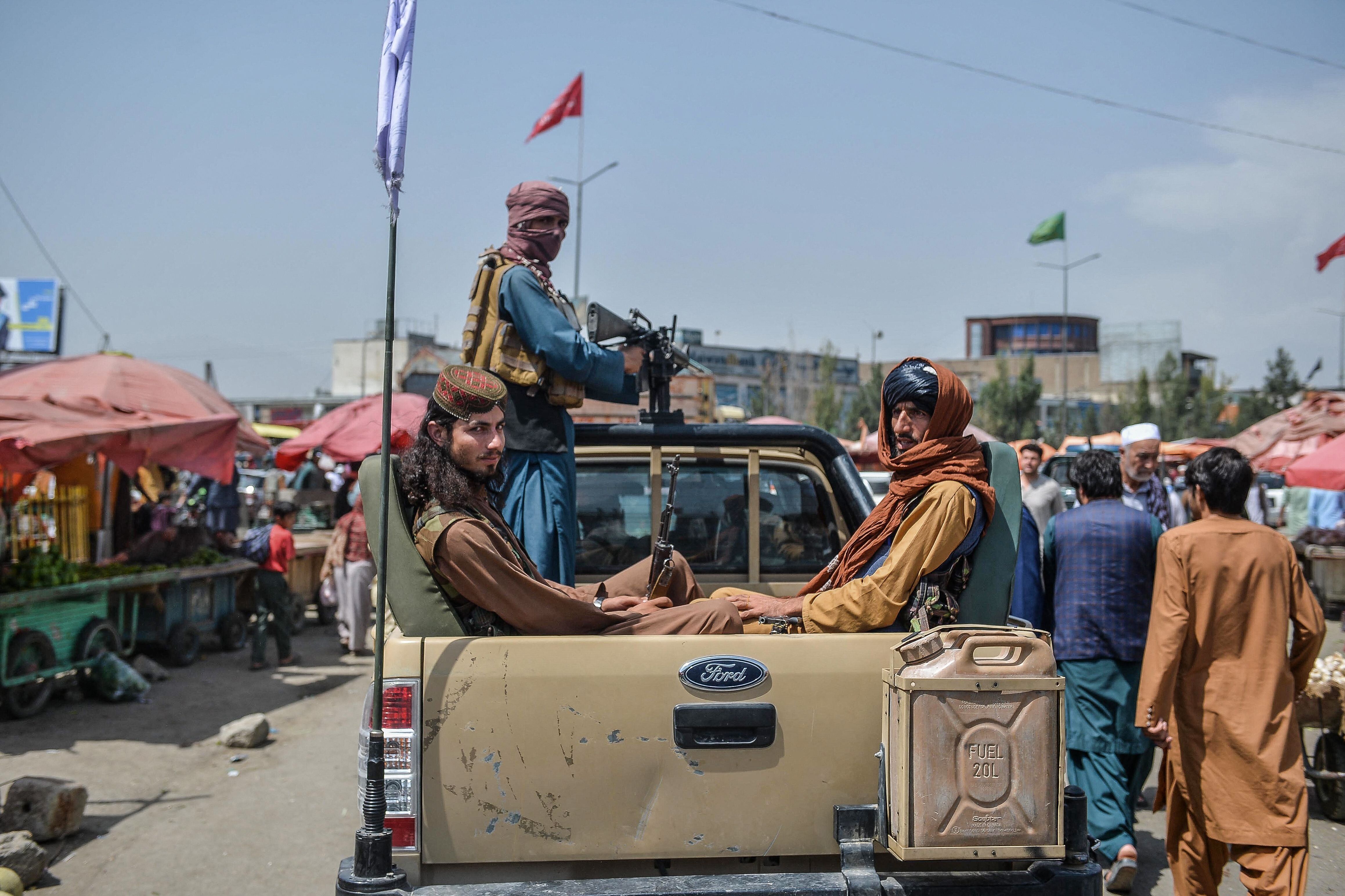 Taliban fighters on a pick-up truck move around a market area, flocked with local Afghan people at the Kote Sangi area of Kab
