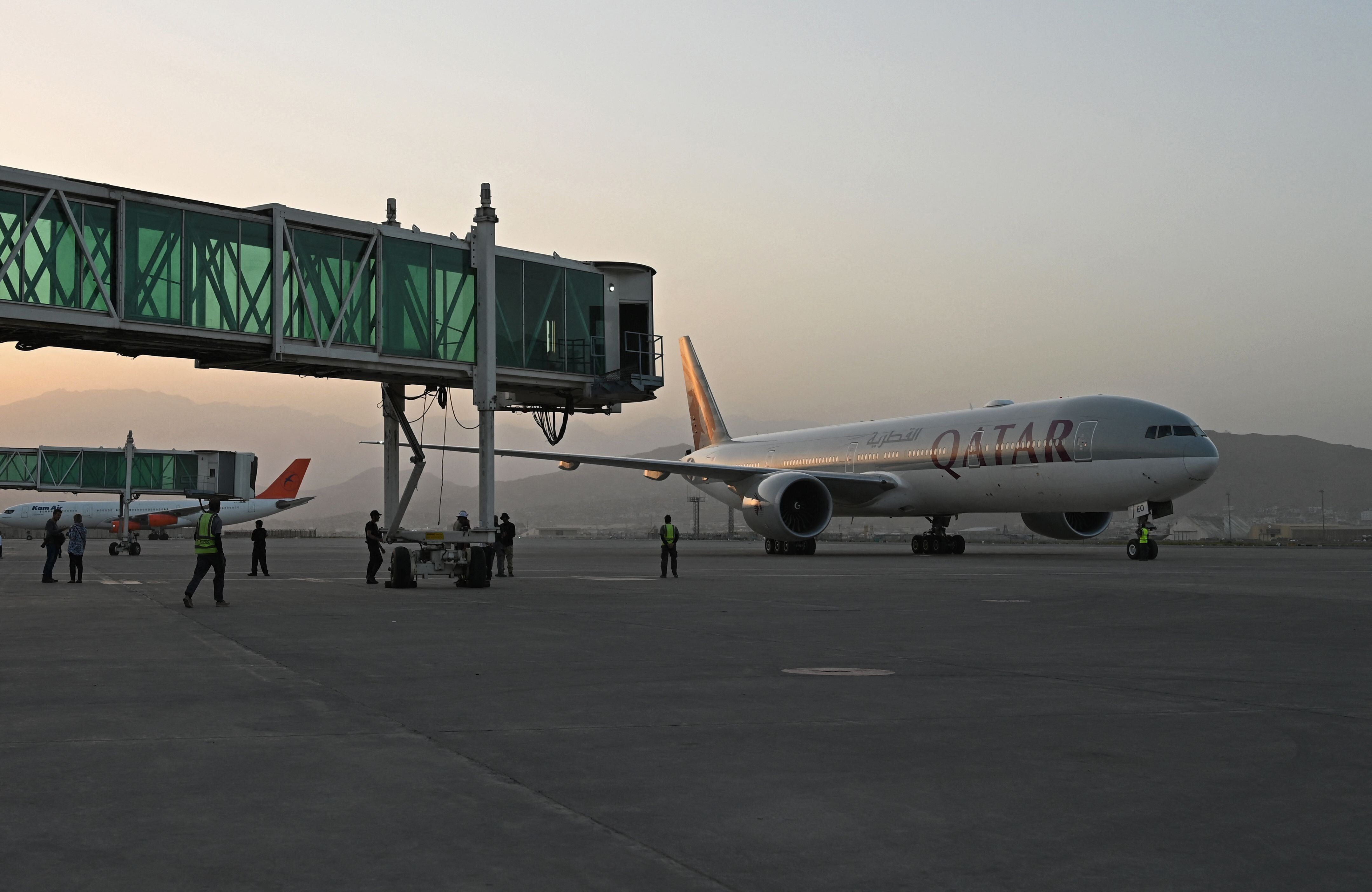 Members of ground staff stand on the tarmac as a Qatar Airways aircraft taxis before taking off from the airport in Kabul on 