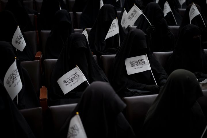 Women wave Taliban flags as they sit inside an auditorium at Kabul University's education center during a demonstration in su