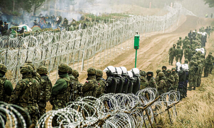 Polish soldiers and police watch migrants at the Poland-Belarus border near Kuznica, Poland, in this photograph released by the Territorial Defence Forces on Nov. 12, 2021. (Irek Dorozanski/DWOT/Handout via Reuters)
