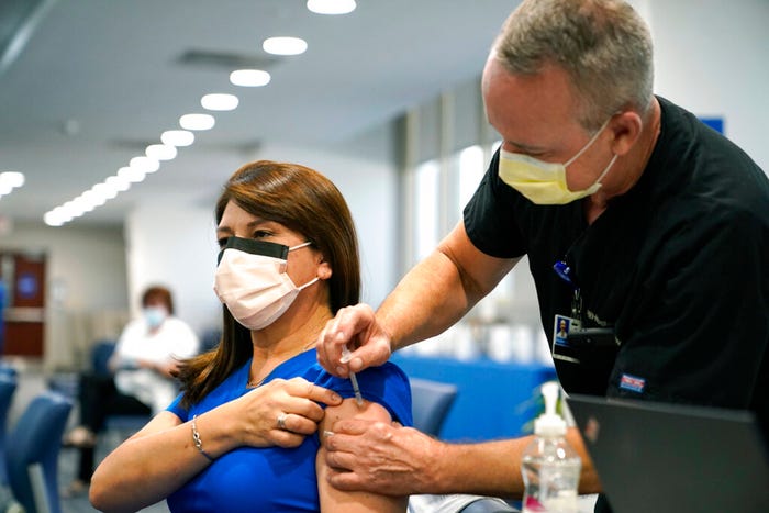 A woman wearing a mask and blue scrubs gets a shot in a clinic.