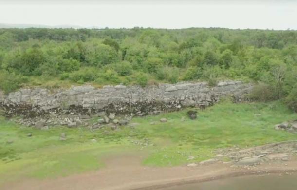 Field archaeologist Michael Gibbons, left, discovered the outlines of this gigantic Bronze Age fortress, partially visible in the background of this image, which may be nearly 3,200 years old, while carrying out routine field work in a nature preserve in County Galway, Ireland.	Source: YouTube screenshot / RTE News