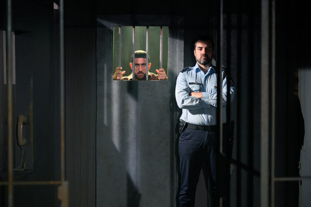 A still from Prisoners of the Occupation in Denmark, with Arian Kashef (l) and Martin Hylander (r). The scene shows an Israeli prison guard standing in front a cell with a Palestinian prison looks out from behind bars. (Photo by Søren Meisner of Teater Gaius)