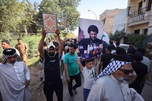 A Supporter of Moqtada Sadr raises a picture of the Shiite Muslim leader, as another carries a Quran, during a demonstration outside the Swedish embassy in Baghdad, after they breached the building briefly over the burning of the Quran by an Iraqi living in Sweden, on June 29, 2023. [AHMAD AL-RUBAYE/AFP via Getty Images]
