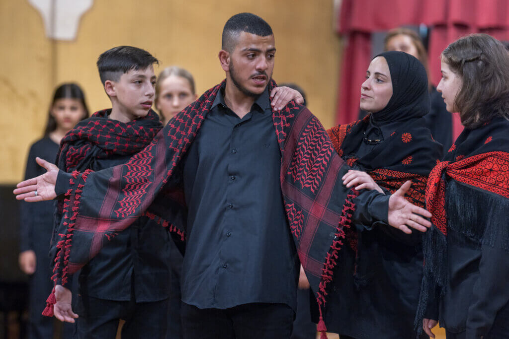 In the opera Amal — Oltre il Muro, siblings are on a quest to reach their father in prison. Left-to-right of the in-focus figures: Rami, played by Yacoub; Sabri, played by Mohammad; Amal, played by Lina; Faizah, played by Tala. All are from Hebron. (Photo: Fares S. Mansour)